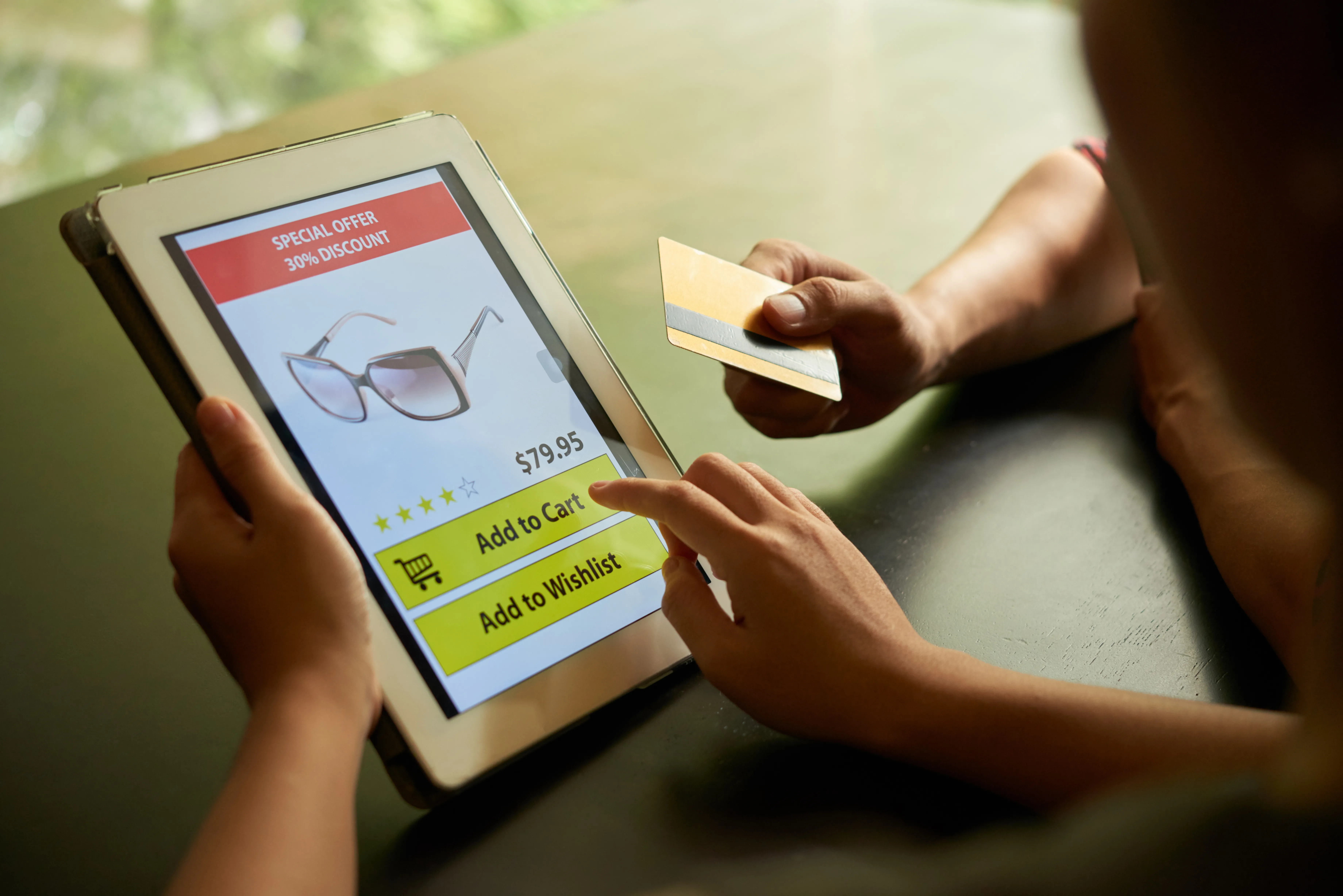 Hand holding credit card near tablet purchasing discounted sunglasses