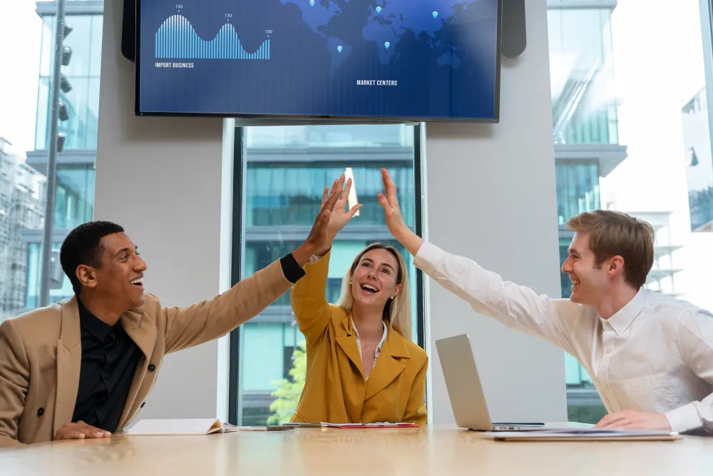 Diverse team celebrating with high-fives in modern office meeting.