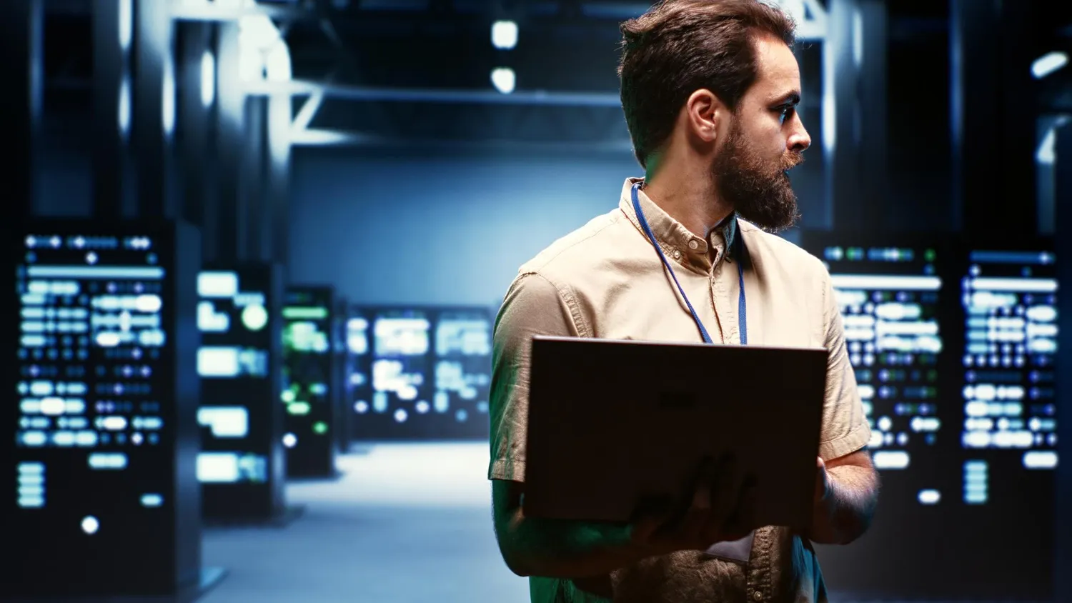Technician in a data center holding a laptop with server racks and blue lighting in the background.