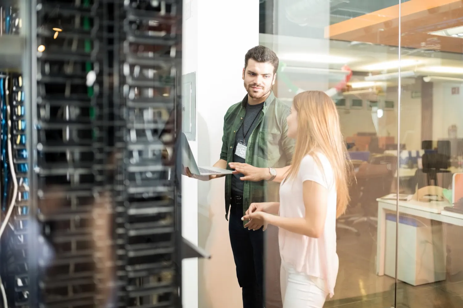 Two IT professionals discussing in a server room with a laptop.