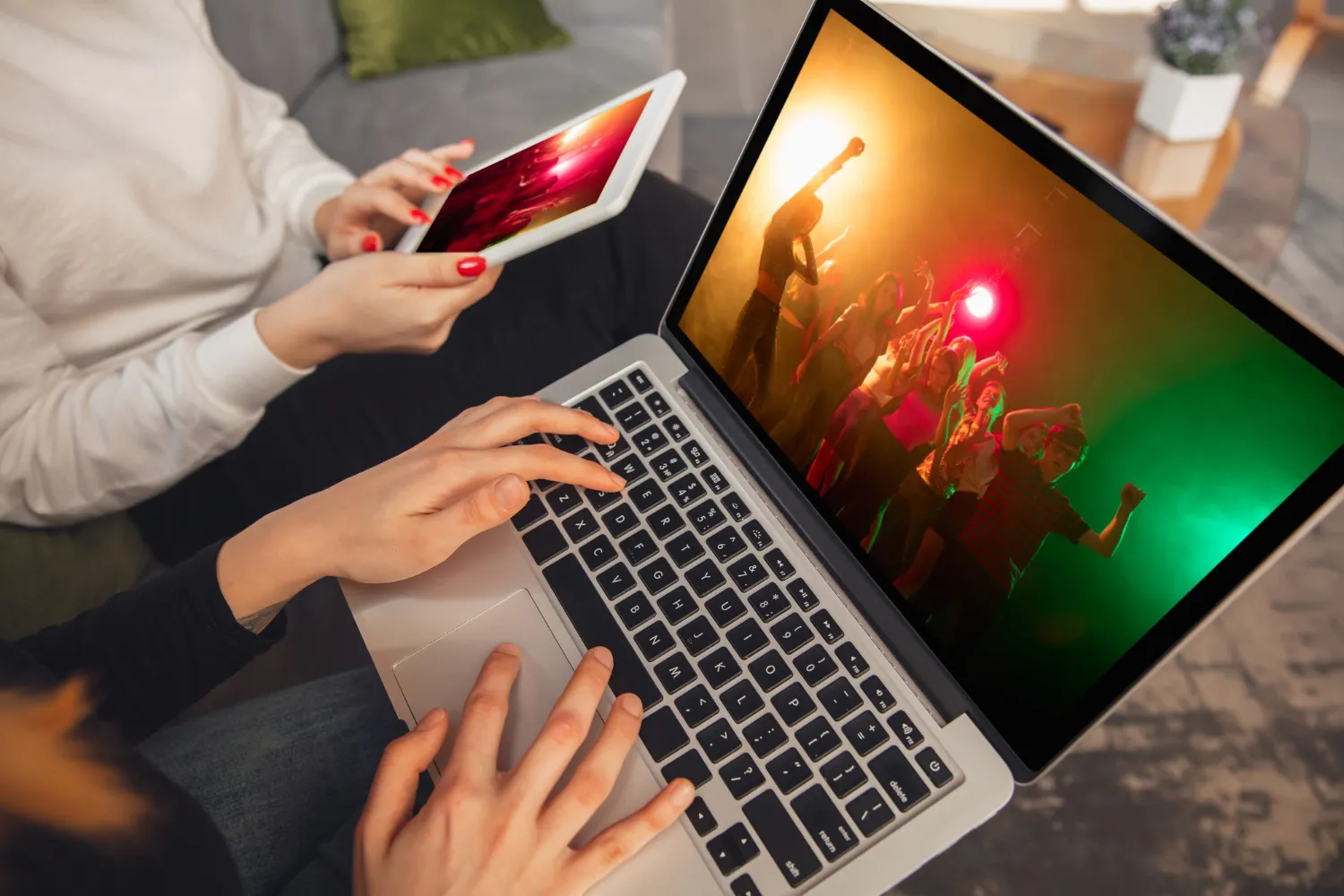 People watching a party video on a laptop and tablet, showing a scene with a crowd dancing and colorful lights.