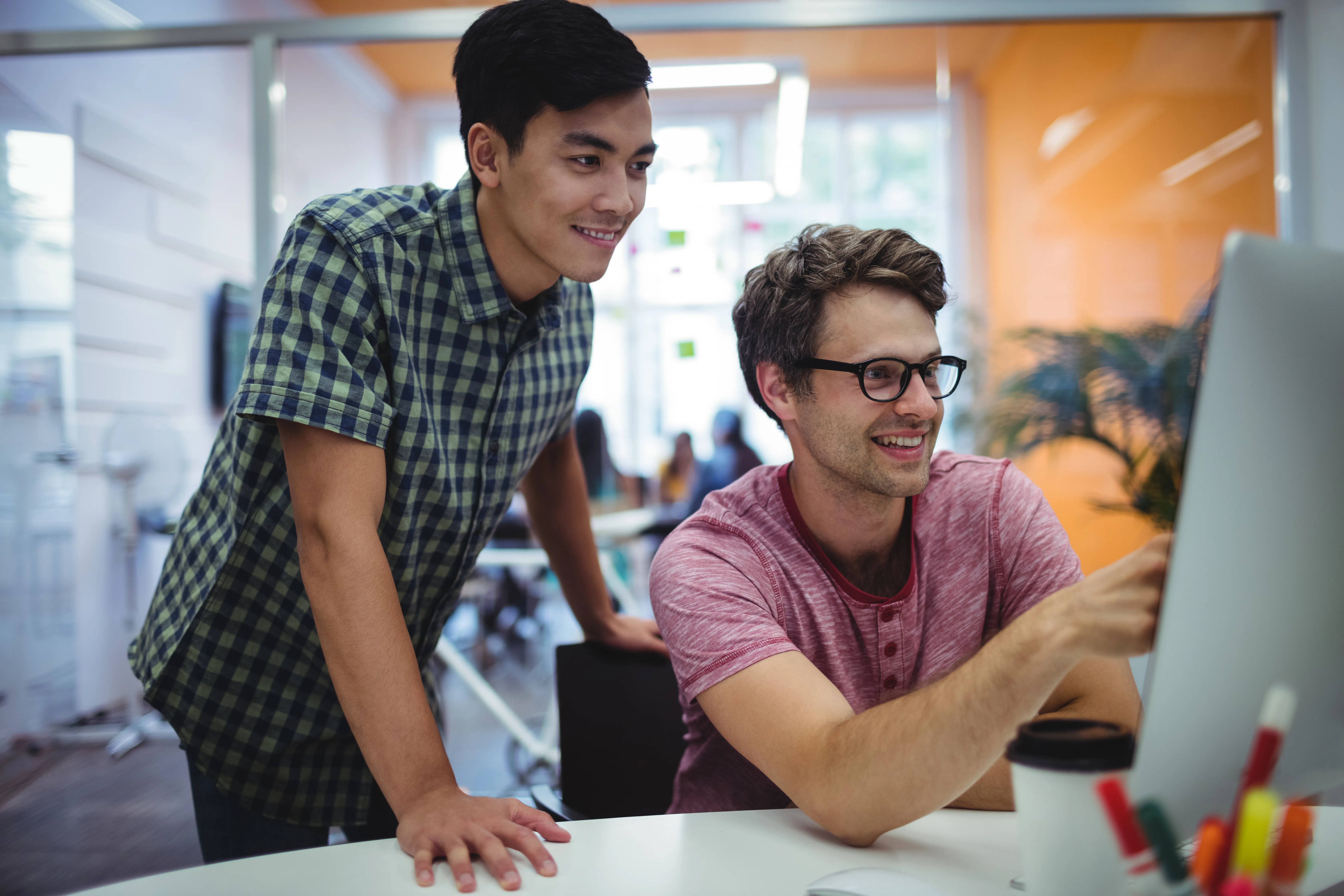 Two colleagues discussing work at computer in modern office.