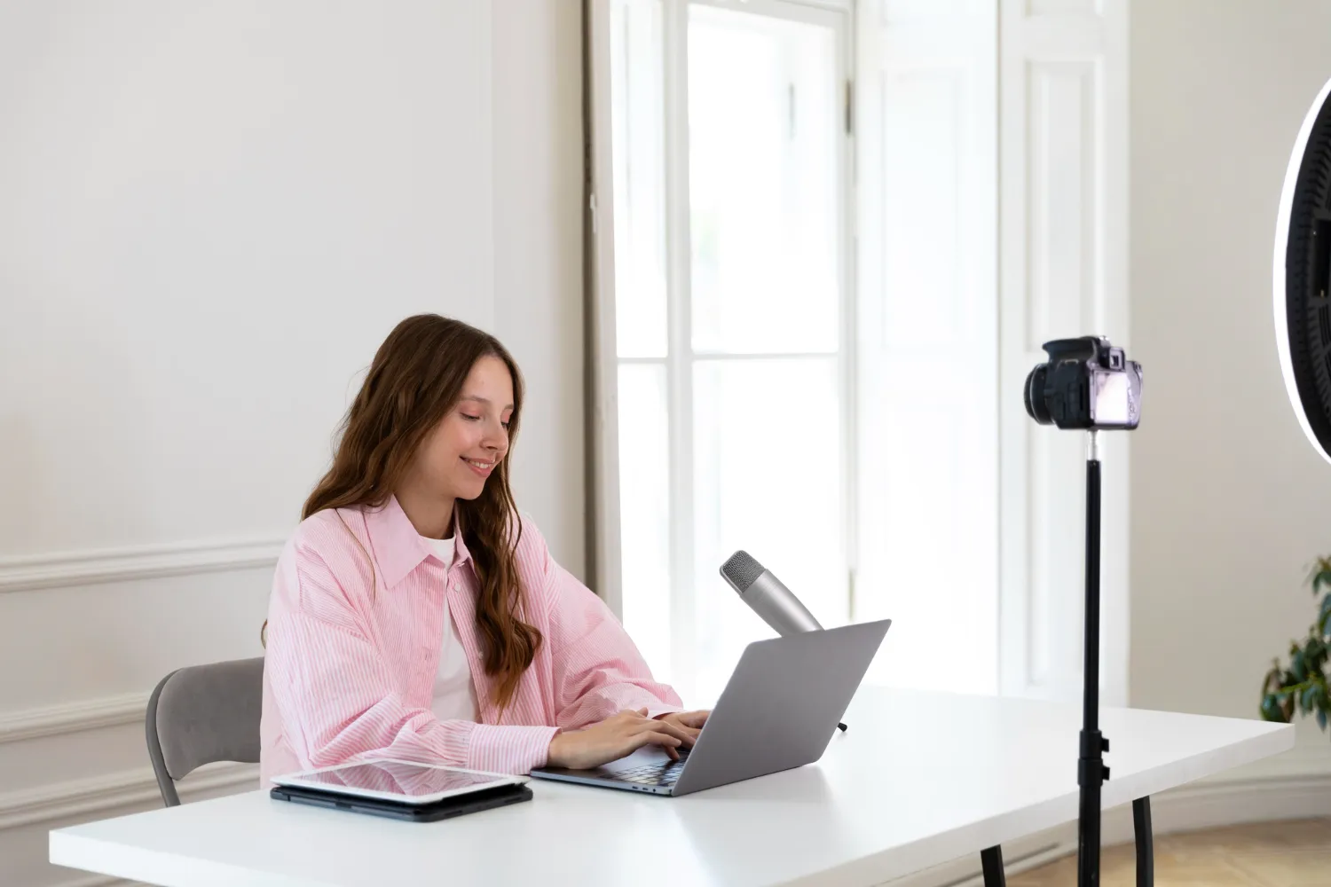 Young woman streaming with professional microphone, ring light, and laptop.