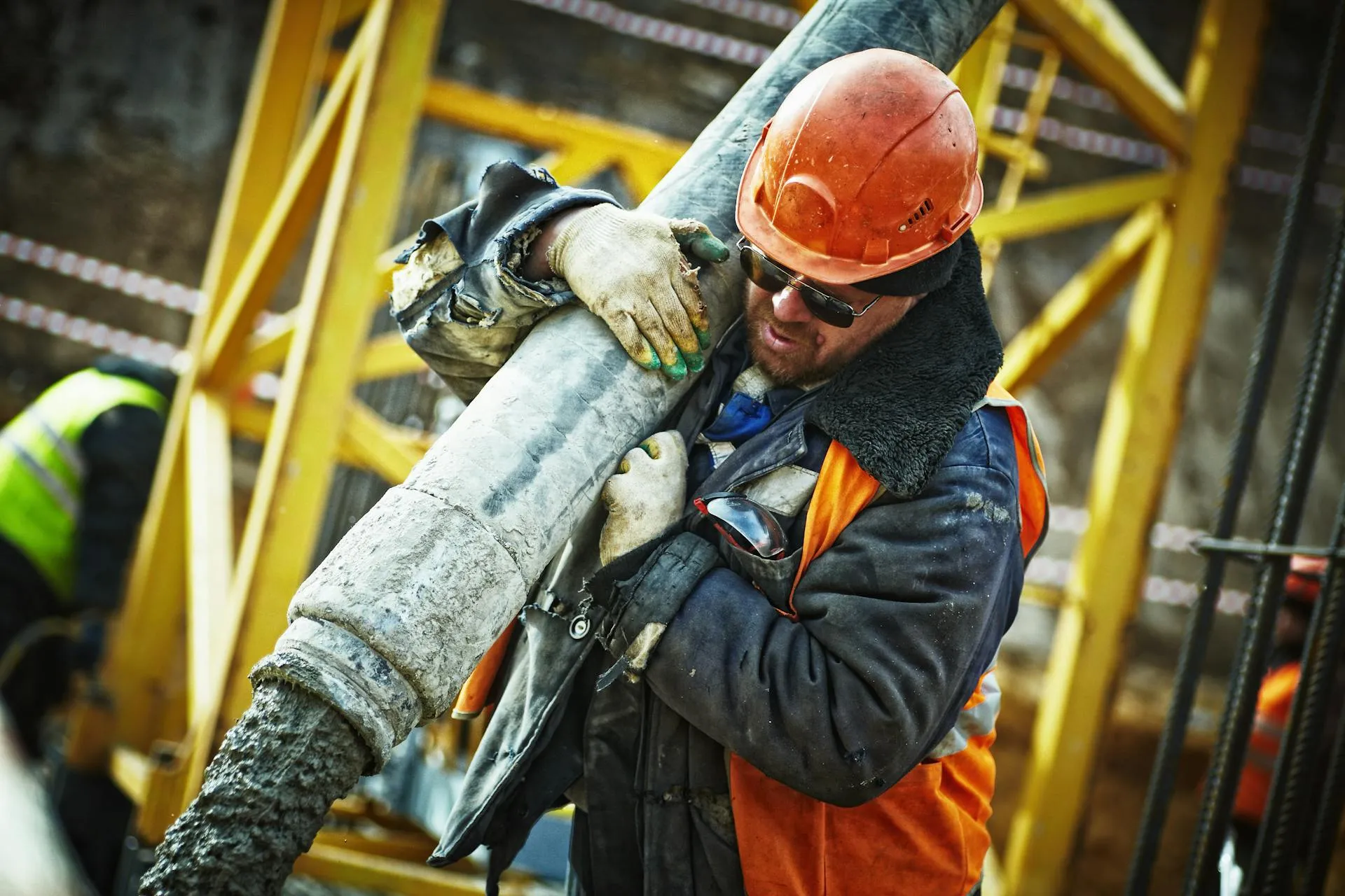 Hard-working construction worker carries hefty concrete pipe at site.