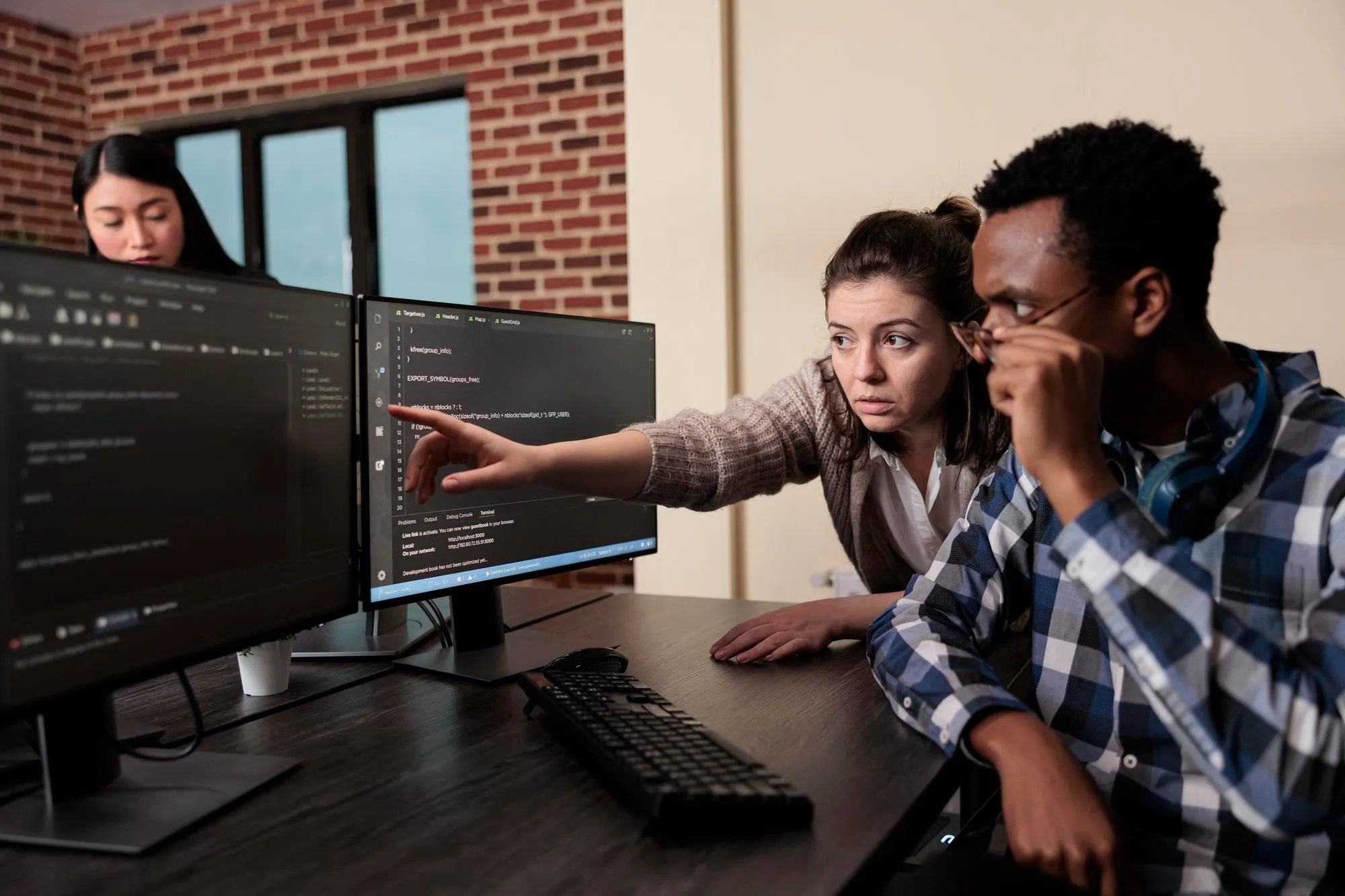 eam collaborating on coding project, pointing at computer screens.