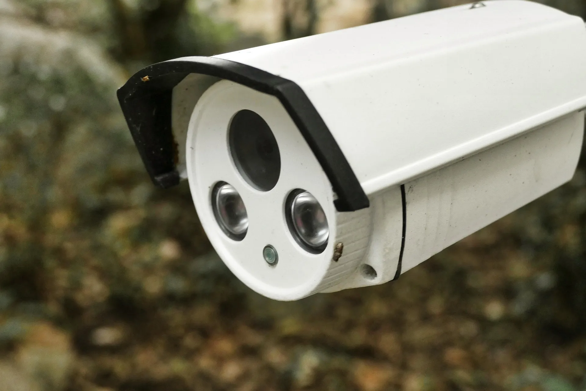 Closeup of white outdoor security camera with three lenses mounted on wall, showing detail of surveillance equipment