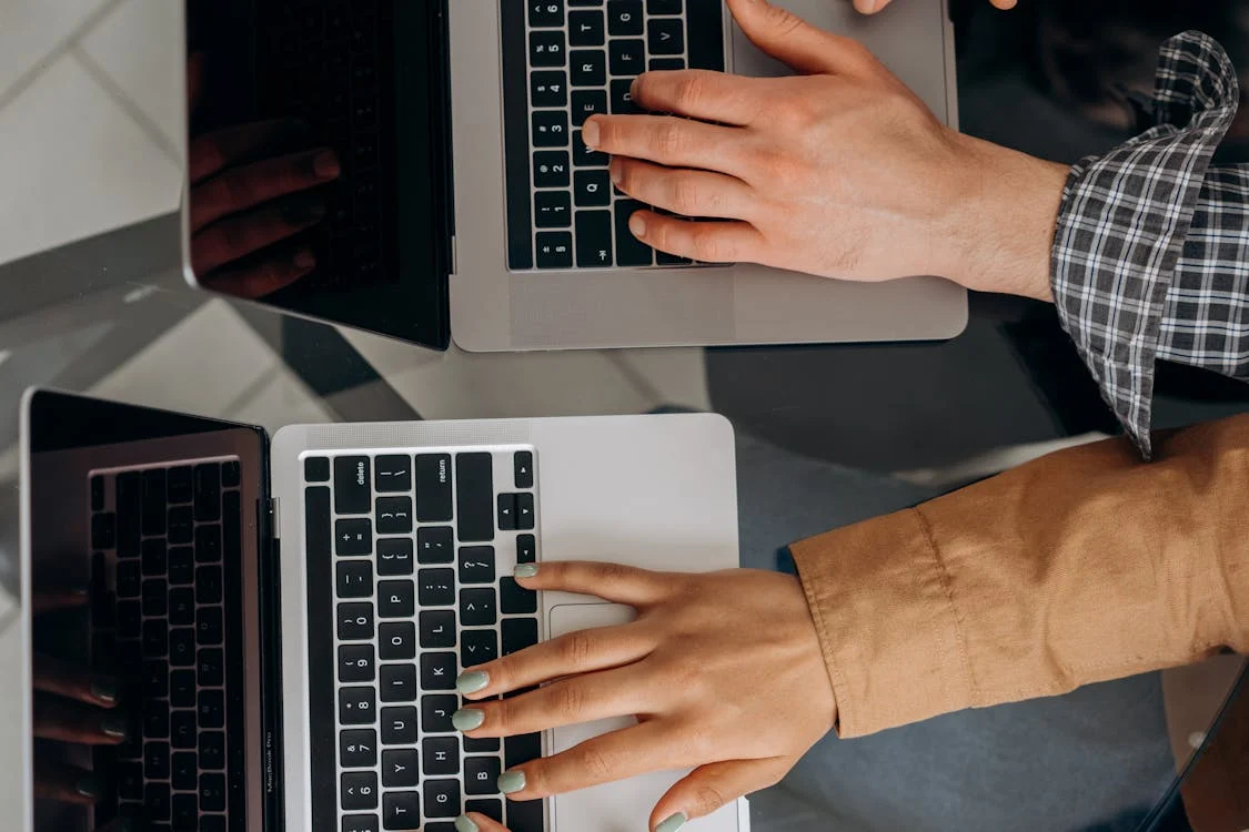 Two people collaborating on laptops, typing on keyboards together.