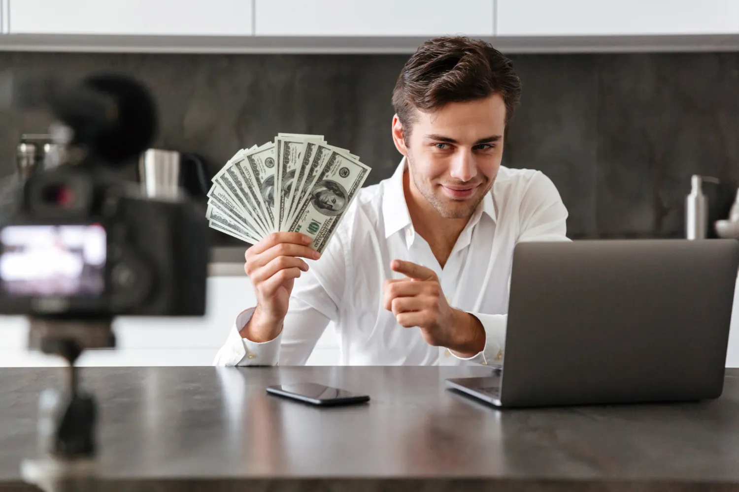 Man holding cash, working on laptop, recording video content.