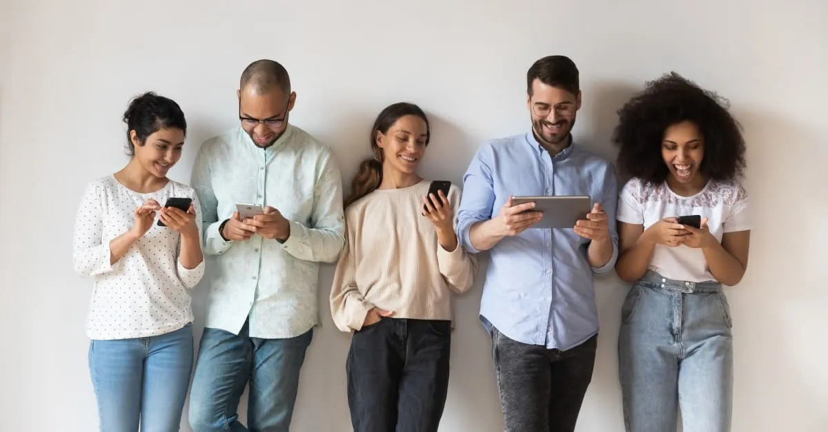 Five people smiling while using phones and tablet on white background.