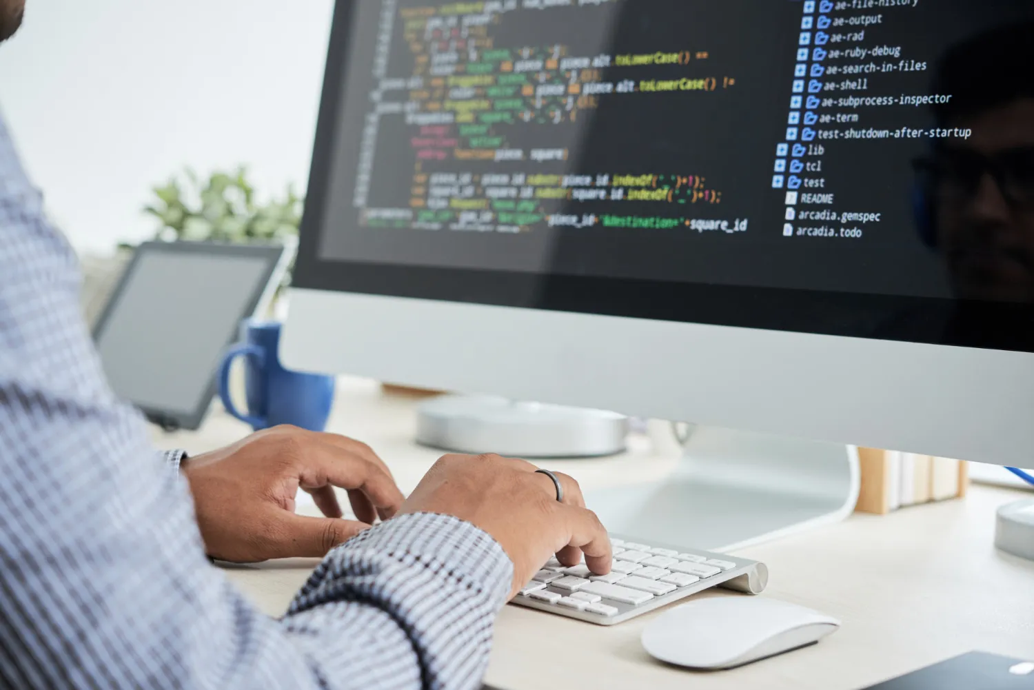 Person typing code on a desktop computer screen.