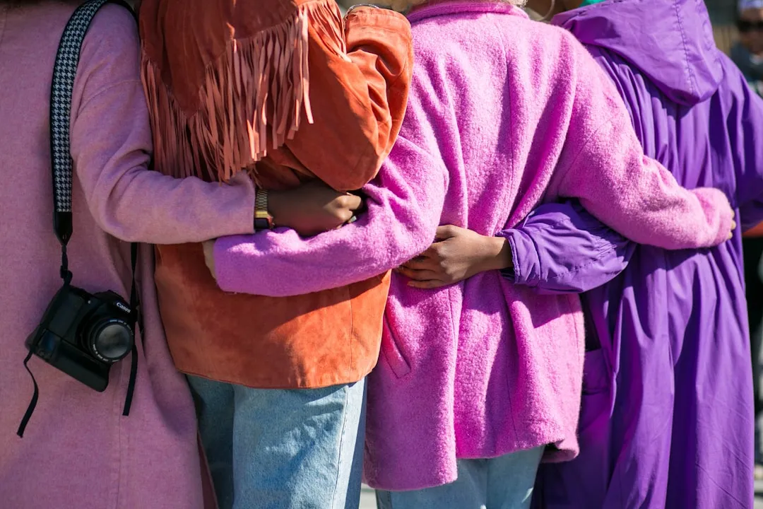 Close-up of friends hugging in vibrant pink and purple coats.