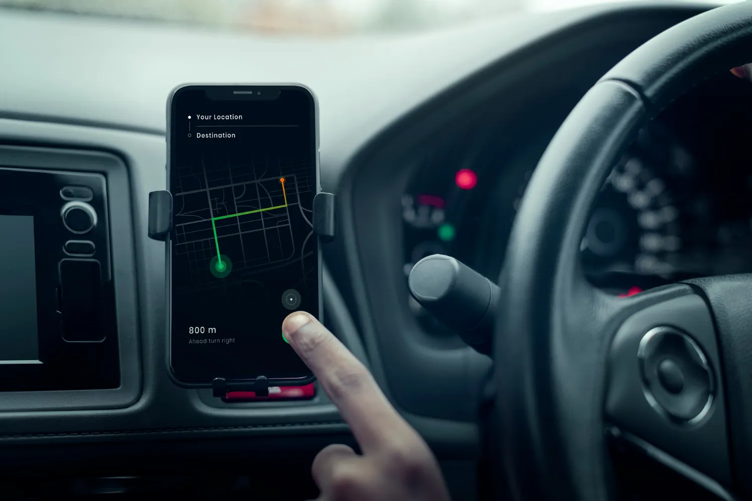 A driver using a navigation app on a smartphone mounted on the dashboard, showing a route with turn-by-turn directions