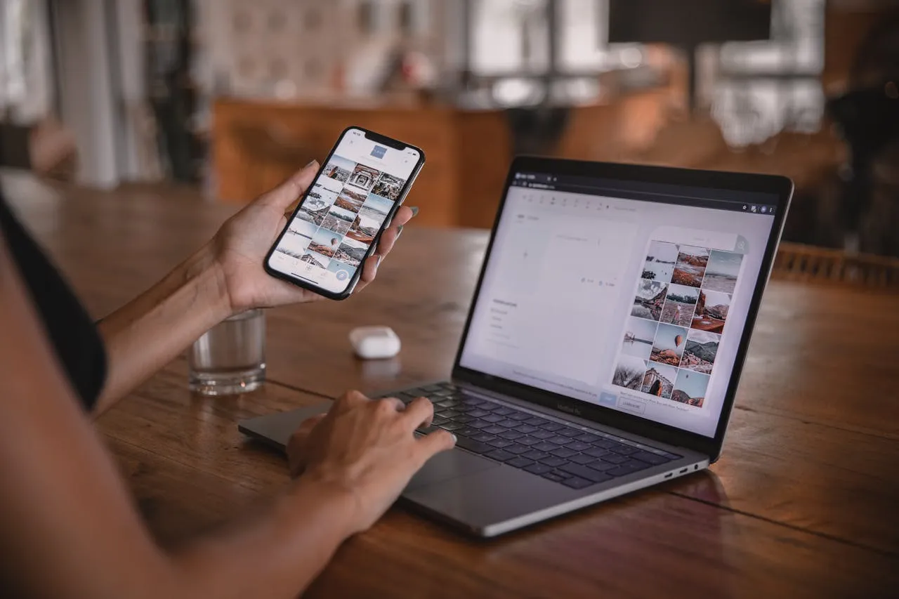 Hands editing photos on phone and laptop at wooden desk