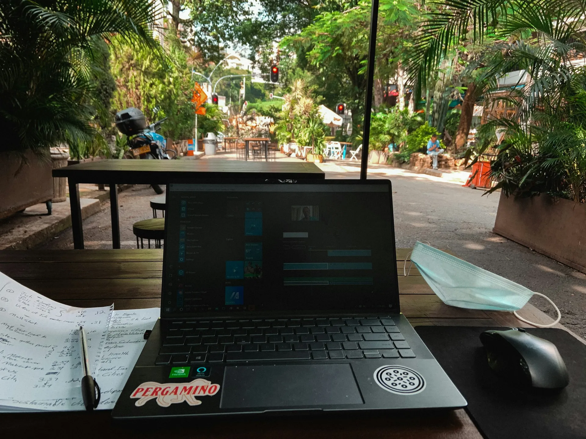 Person working remotely on laptop at sunny outdoor cafe table.