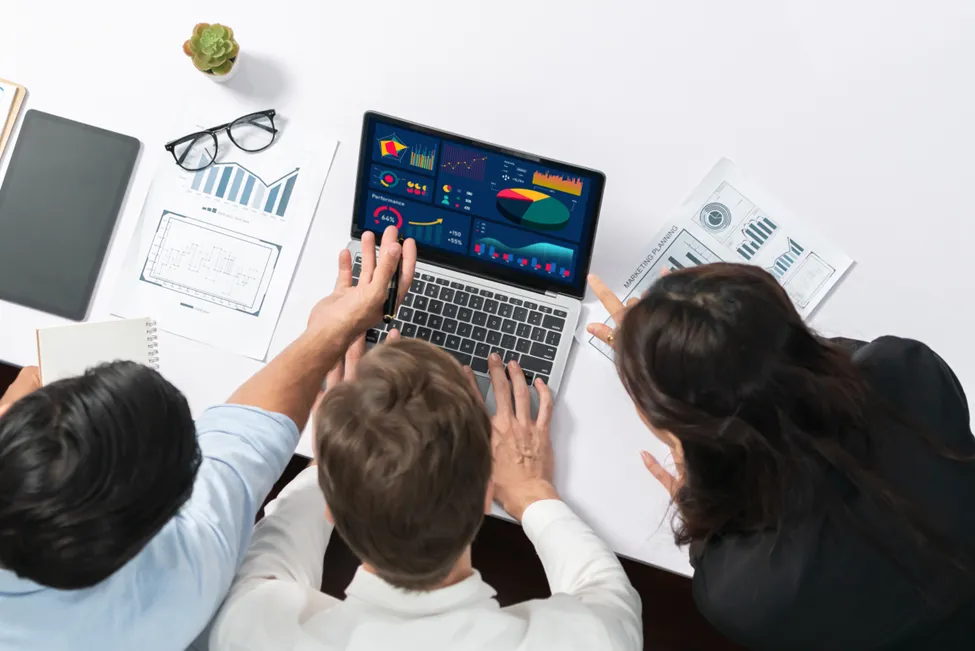 Business team analyzing data dashboards on a laptop with charts and marketing plans on the table.