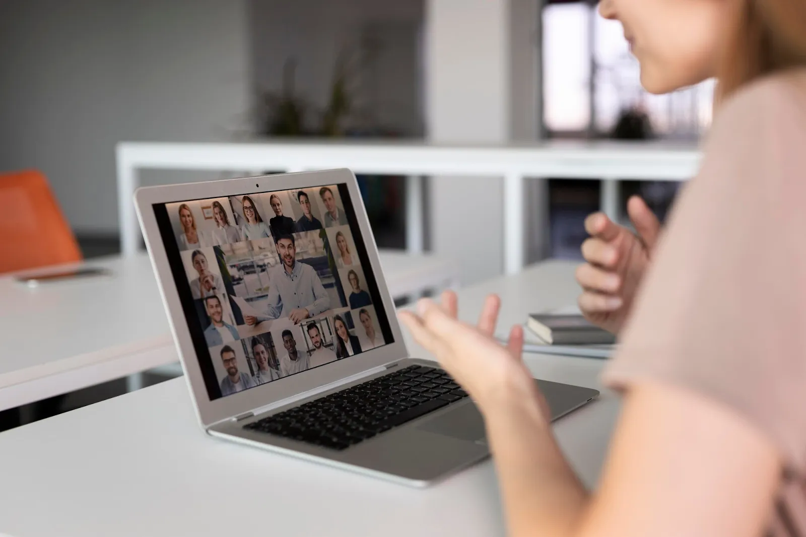 Person gesturing while on video call with multiple participants visible on laptop screen