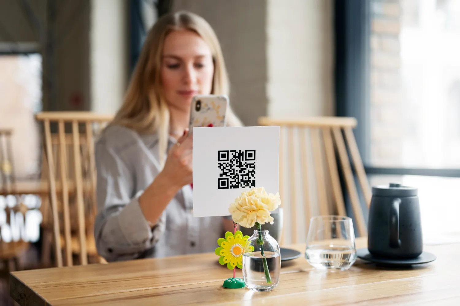 Woman sitting at a café table scanning a QR code with her smartphone, showcasing digital ordering or payment system.