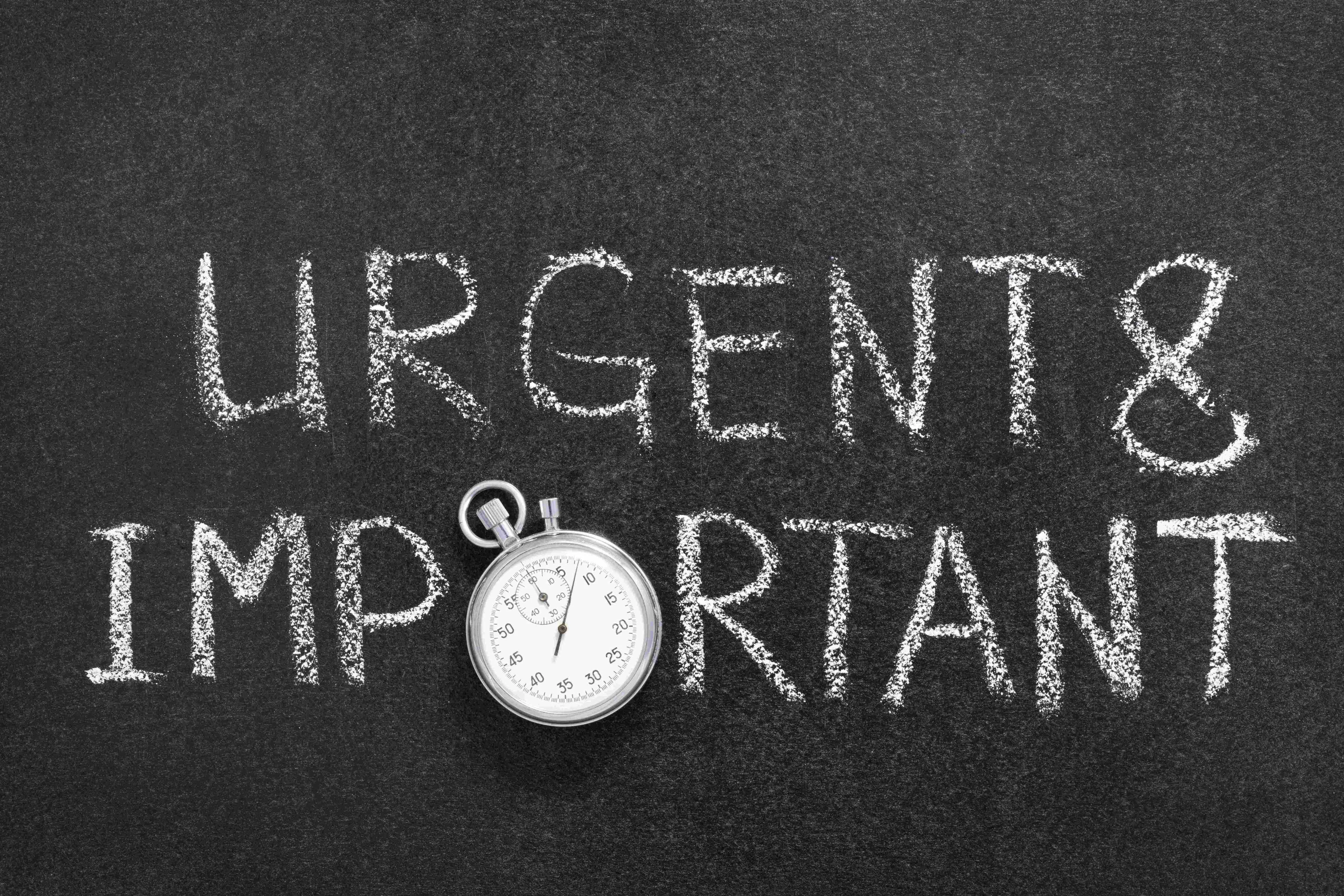 Chalkboard with 'Urgent & Important' written in chalk and a stopwatch placed below the writing.