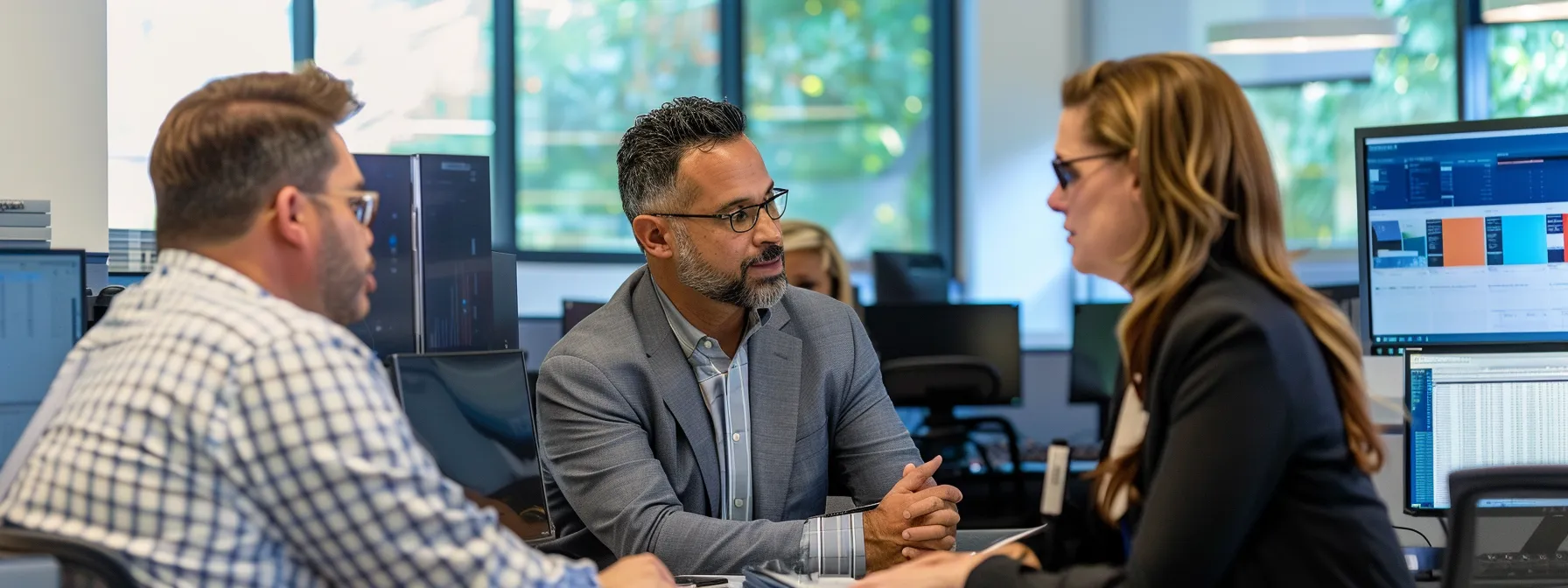 Three individuals at a table, focused on computer monitors, collaborating on knowledge management in finance.