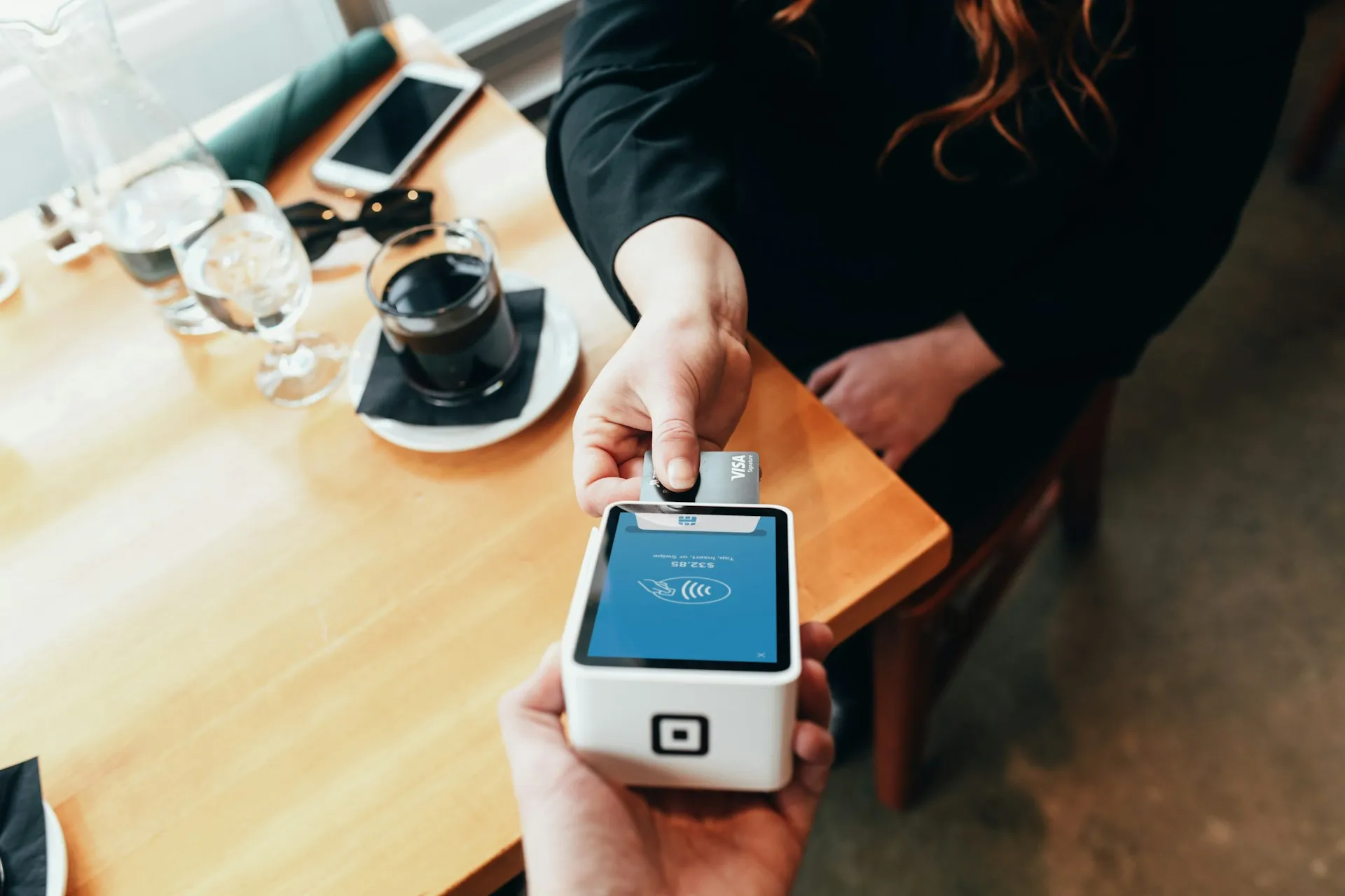 Close-up of a customer making a contactless payment using a credit card on a portable card reader at a coffee shop.