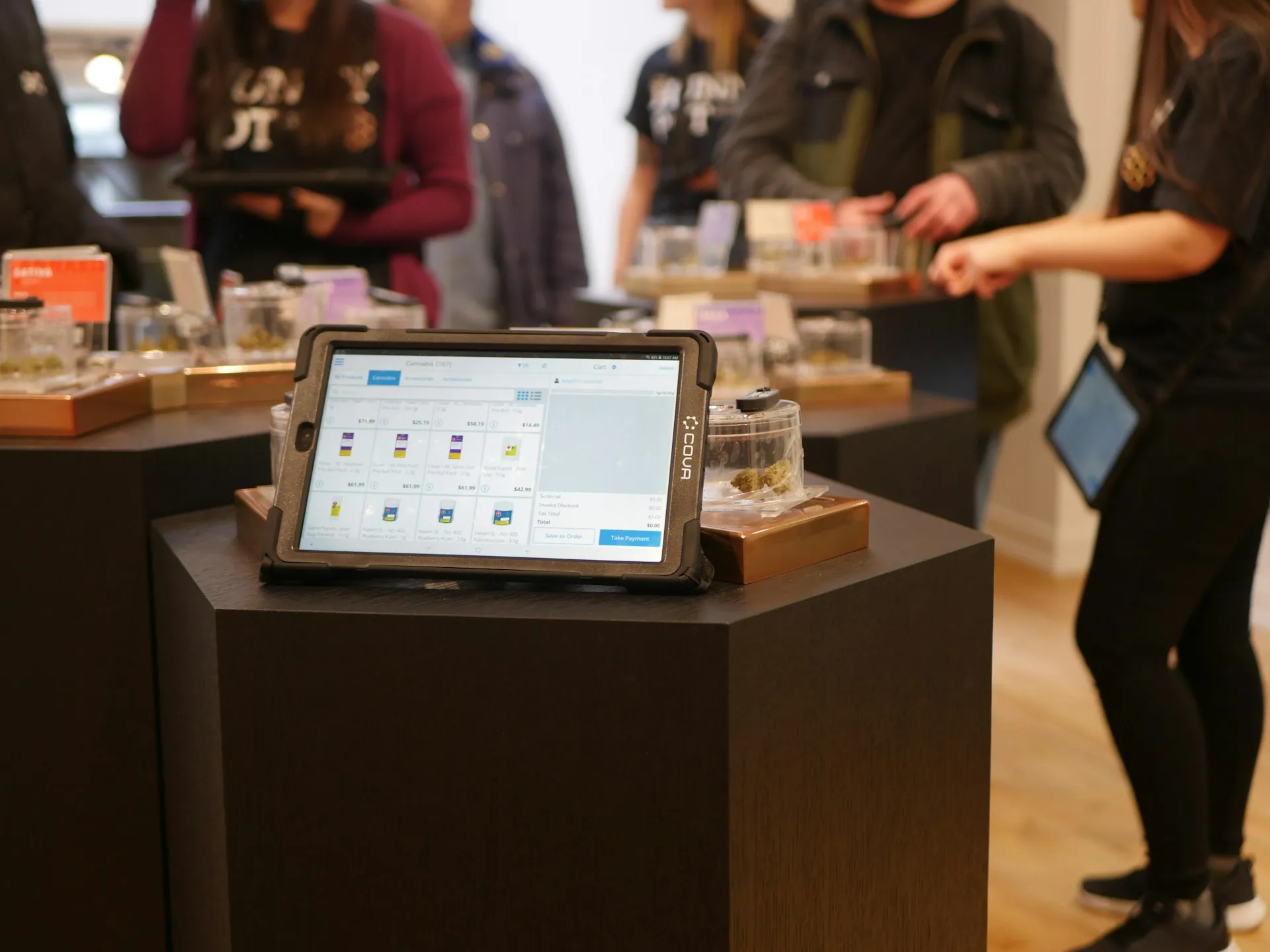 Tablet displaying an ordering system in a retail store, with customers browsing in the background.