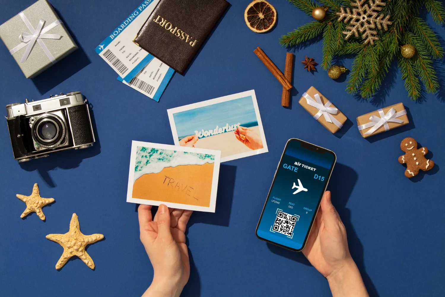 Flat lay of travel essentials including a passport, boarding pass, vintage camera, smartphone with digital air ticket, postcards, starfish, gift boxes, and holiday decorations on a blue background.